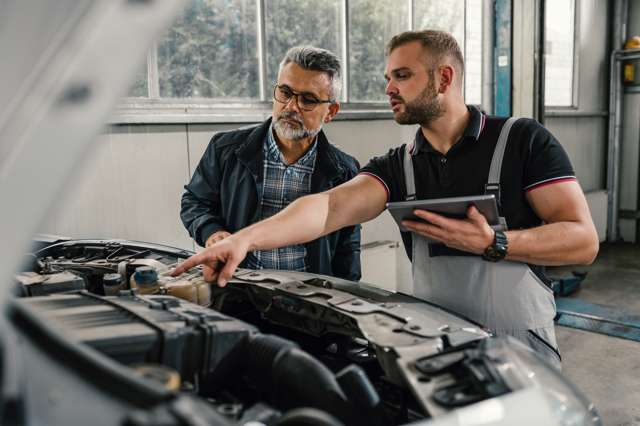 Mechanic standing beside customer as he points to the car engine